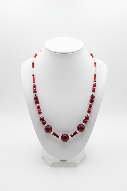 A red beaded necklace displayed on a white jewelry bust against a light gray studio background.