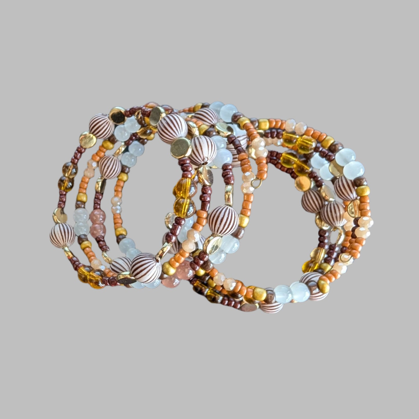 This elegant memory wire bracelet features four coils adorned with brown, white, and tan beads, complemented by gold, brown, and tan spacer beads. Its versatile color palette pairs effortlessly with any outfit, while the flexible design ensures a comfortable fit for all wrist sizes. Add a touch of sophistication and warmth to your look with this stylish accessory.