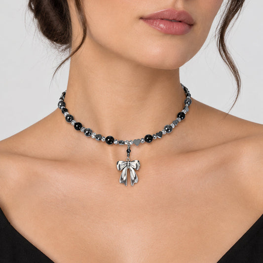 A close-up of a woman wearing a beaded choker necklace with a silver bow pendant. The necklace features alternating black and silver faceted beads, with a silver bow charm hanging at the center.