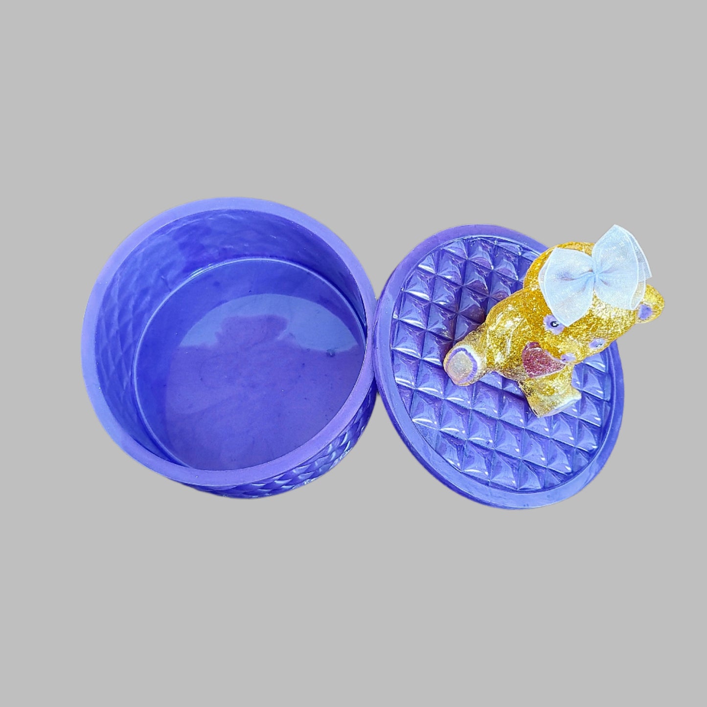 This adorable hand-crafted resin trinket box brings a touch of whimsy to your space! Featuring a charming teddy bear perched on top, it's the perfect home for jewelry, keepsakes, or small treasures. Measuring 5" x 5" x 5" with a 2" deep dish, this compact beauty combines functionality with personality. Crafted from smooth, durable epoxy resin that feels like glass, it's built to last while adding a playful accent to any dresser or shelf. At just 13 oz, it's lightweight enough to move around but sturdy enoug