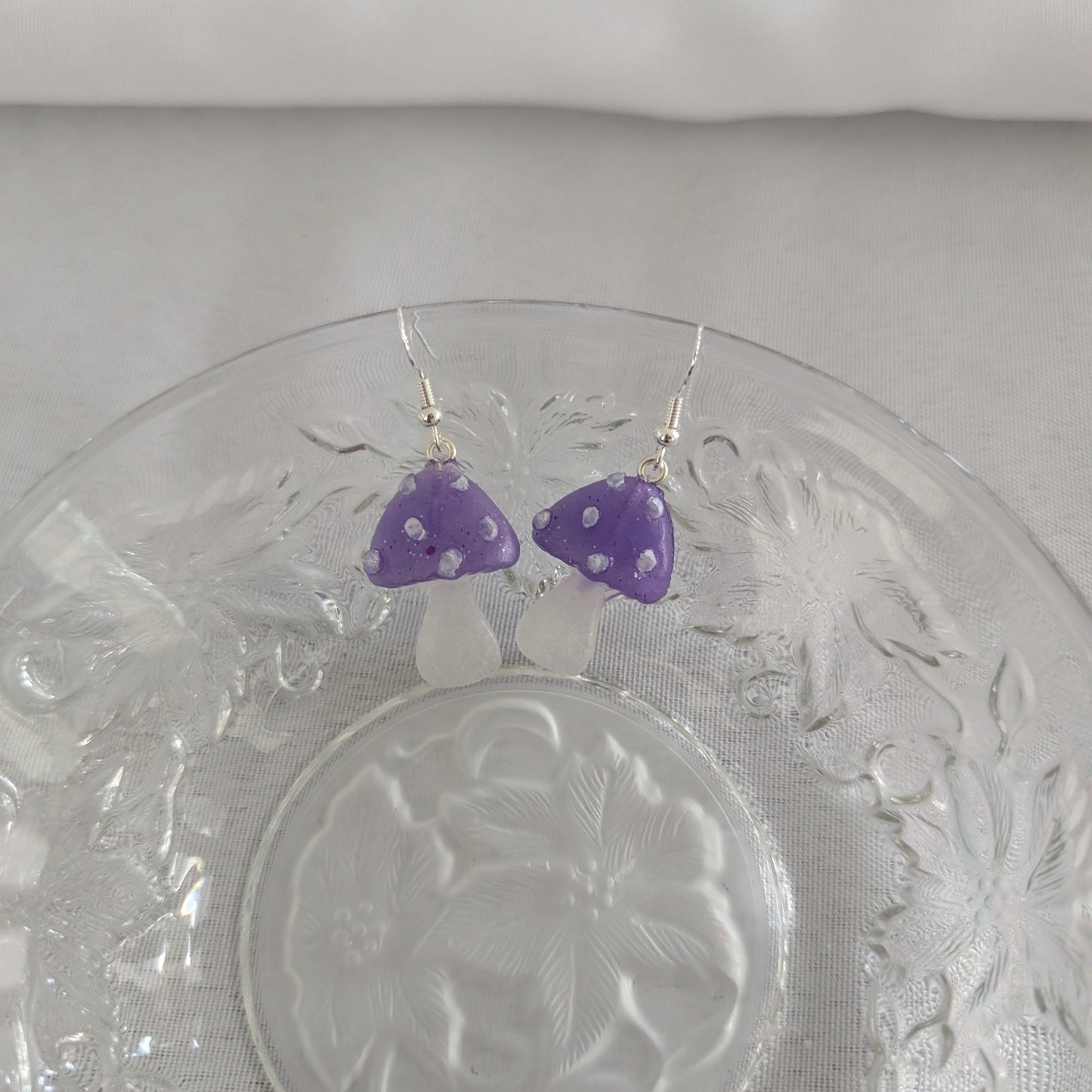 Purple mushroom-shaped earrings on a glass plate with a white background