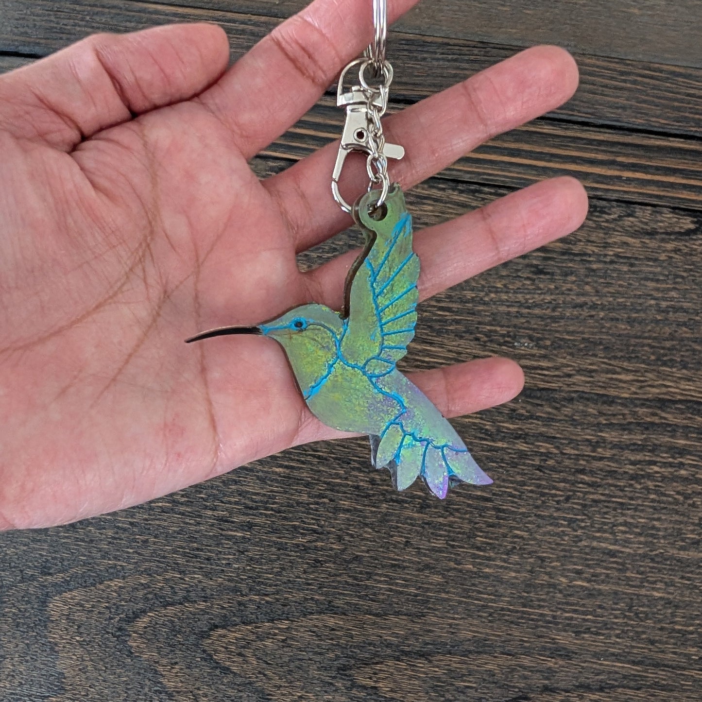 Hand holding a hummingbird-shaped keychain on a wooden surface