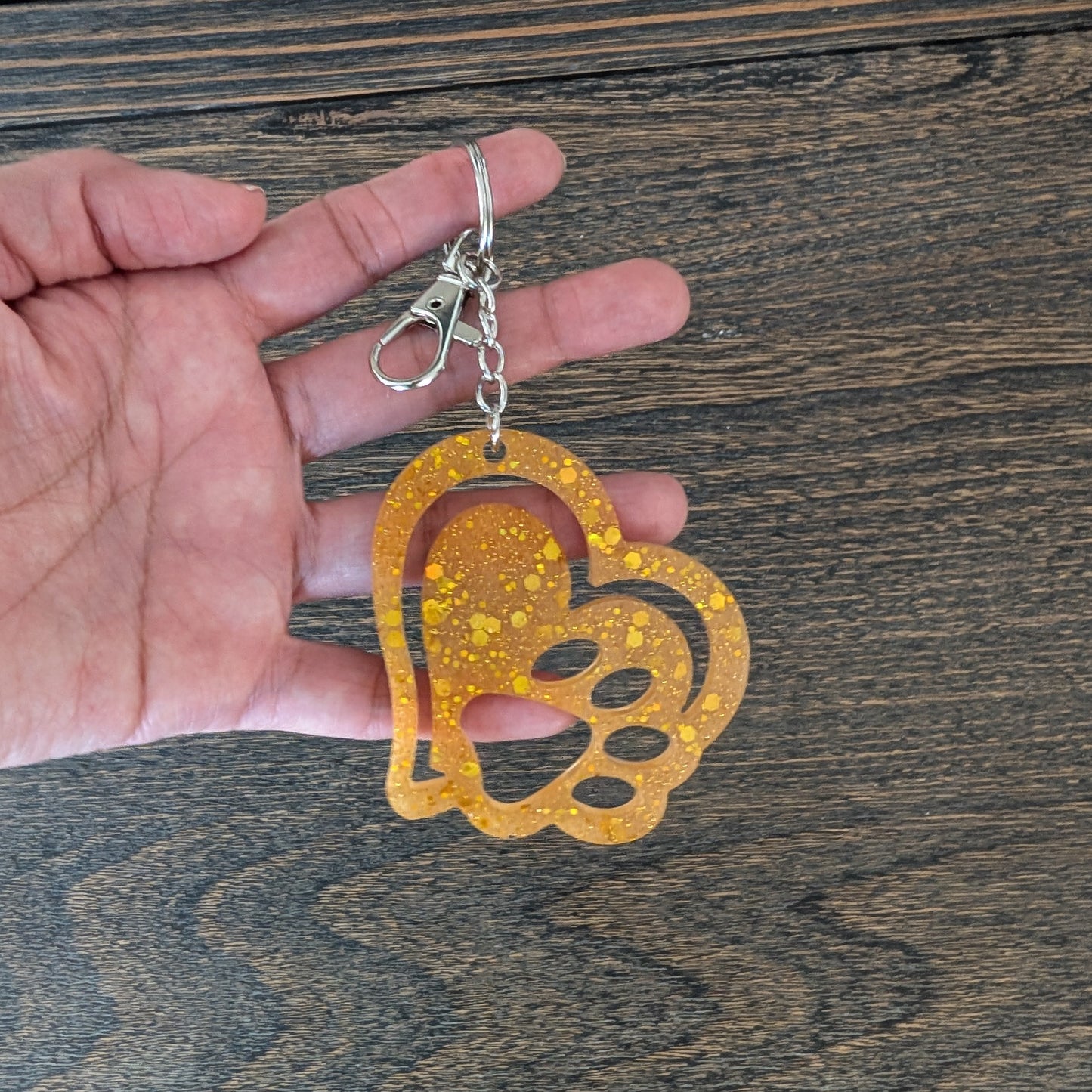 Hand holding a decorative keychain with a heart and paw print design on a wooden surface