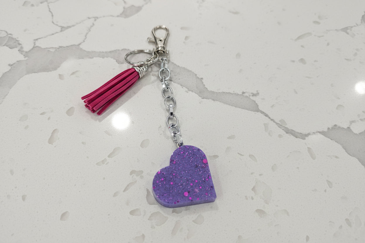 Purple heart-shaped keychain with a pink tassel on a dark surface