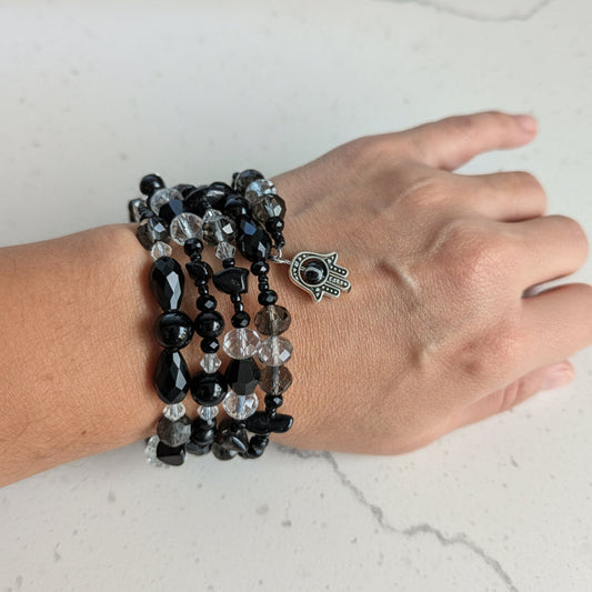 Hand wearing a 4 coil black and clear beaded bracelet on a light background
