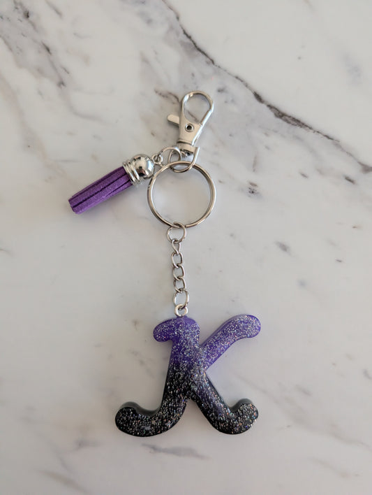 Keychain with letter 'K' in purple and black gradient on a marble background