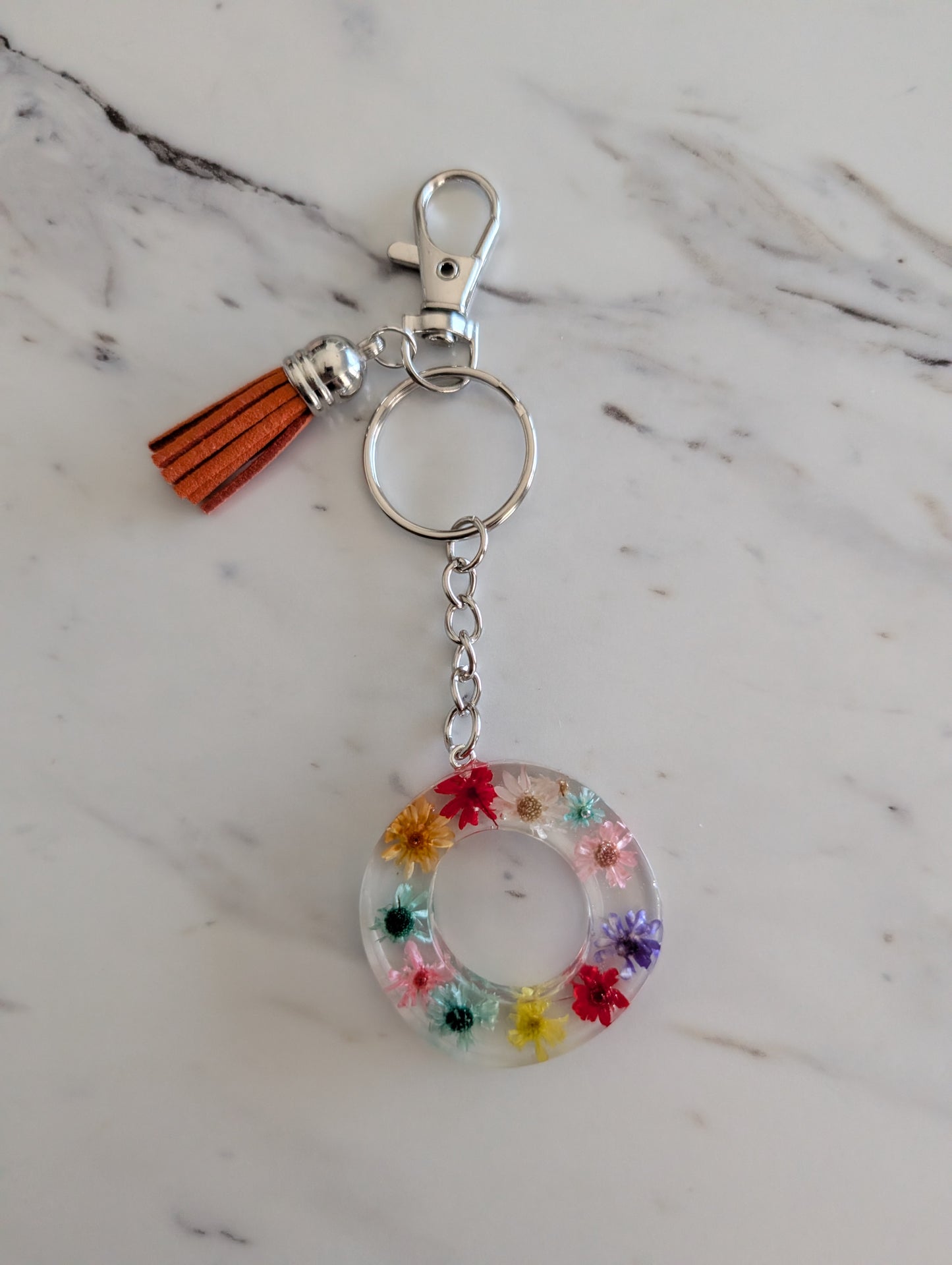 Letter O Keychain with colorful floral design and tassel on a marble surface