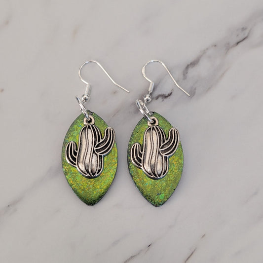 Green leaf-shaped earrings with silver cactus designs on a marble background