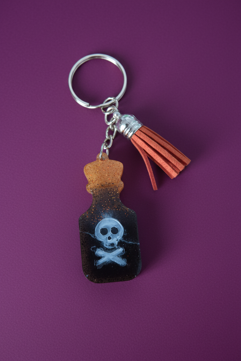A keychain featuring a resin poison bottle with a skull and crossbones symbol, attached to a metal ring and equipped with an acrylic tassel.