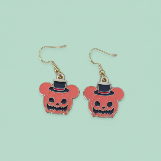 Pumpkin-shaped earrings with top hats on a green background