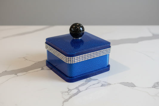 A square-shaped, blue and multicolor resin jewelry box with a lid and diamond-like decorations on the edge.