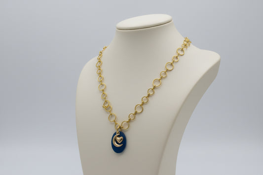 Gold necklace with a blue pendant with a moon heart charm on a mannequin bust against a gray background