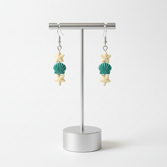 A pair of earrings with starfish and sea shell designs on silver hooks.