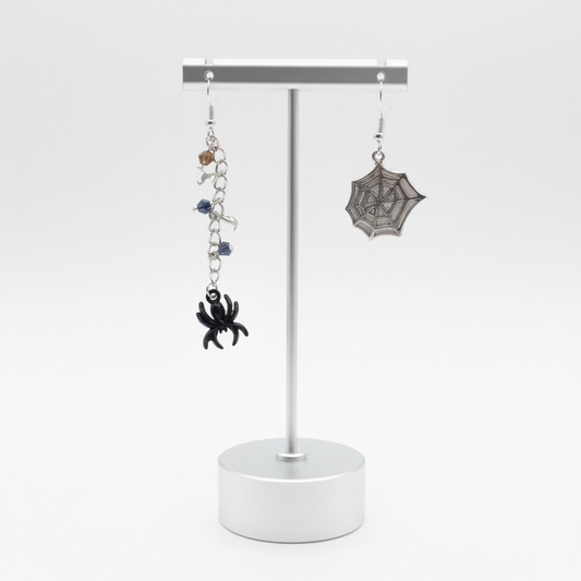 A pair of earrings featuring a black spider on a chain with beads, and a silver spiderweb on the hook.