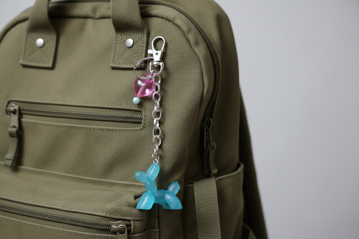 Blue dog-shaped keychain with a pink bead on a backpack