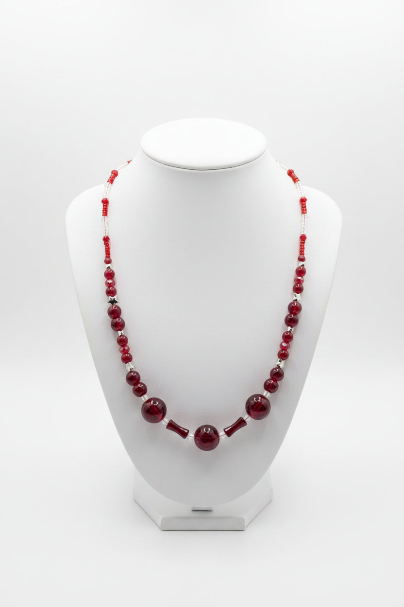 A red beaded necklace displayed on a white jewelry bust against a light gray studio background.