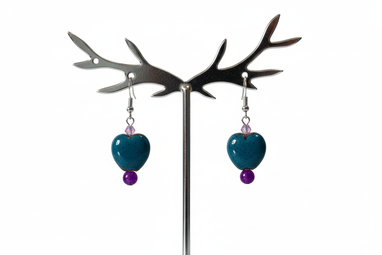 Teal heart-shaped earrings with purple beads on a metal antler stand against a white background
