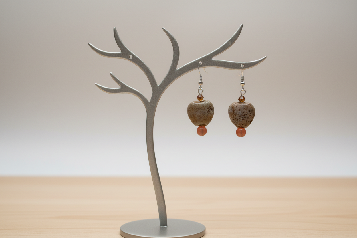 Metal tree-shaped jewelry stand with heart-shaped earrings on a wooden surface.