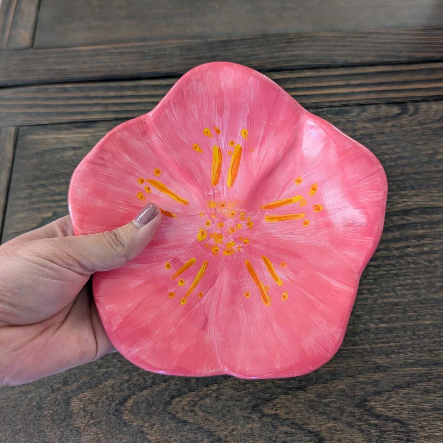 Hand holding a pink flower-shaped object with yellow center on a wooden surface