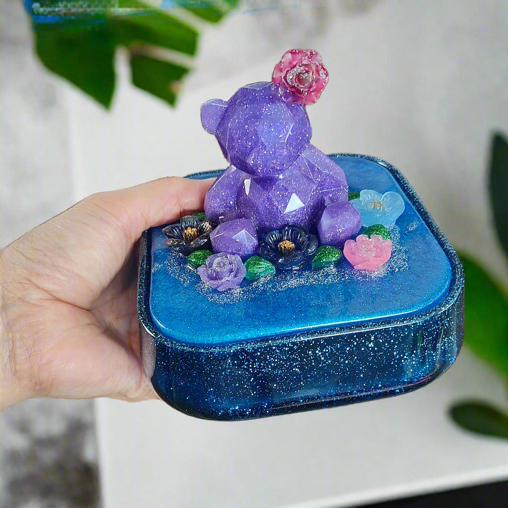 Elevate your jewelry storage with our Knickknack - Large resin square box! Featuring a charming bear and flowers lid, it adds a whimsical touch to any room. Boasting ample space for your precious items, it's the perfect blend of function and beauty. Upgrade to this stunning jewelry box today!