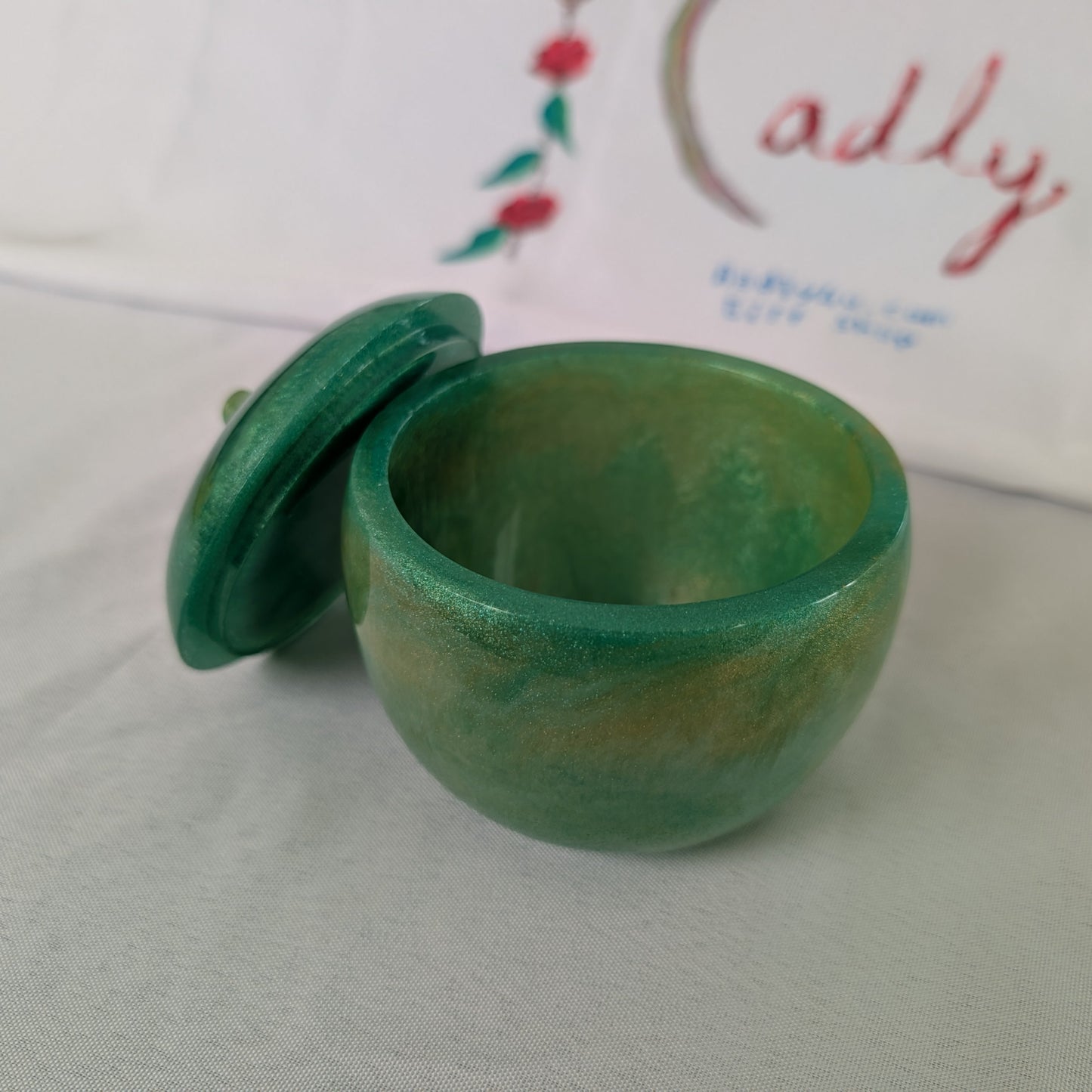 hand crafted with epoxy resin..

Epoxy resin is typically smooth, rigid, and non-porous, similar to a hard plastic or glass.

Knickknack - Resin apple trinket with lid