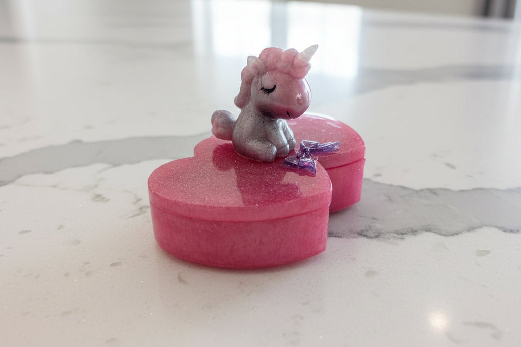 Add a touch of magic to your vanity with this one-of-a-kind, handcrafted epoxy resin trinket box. Featuring a unique double-heart design and topped with an adorable, sleepy unicorn guardian, this box is perfect for storing your most precious rings, earrings, or daily treasures.