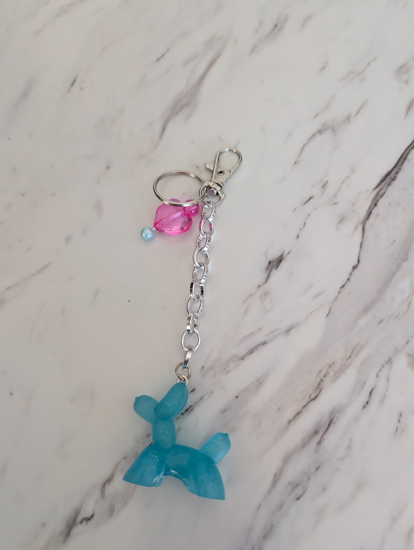 Blue balloon dog charm with pink and blue beads on a marble background