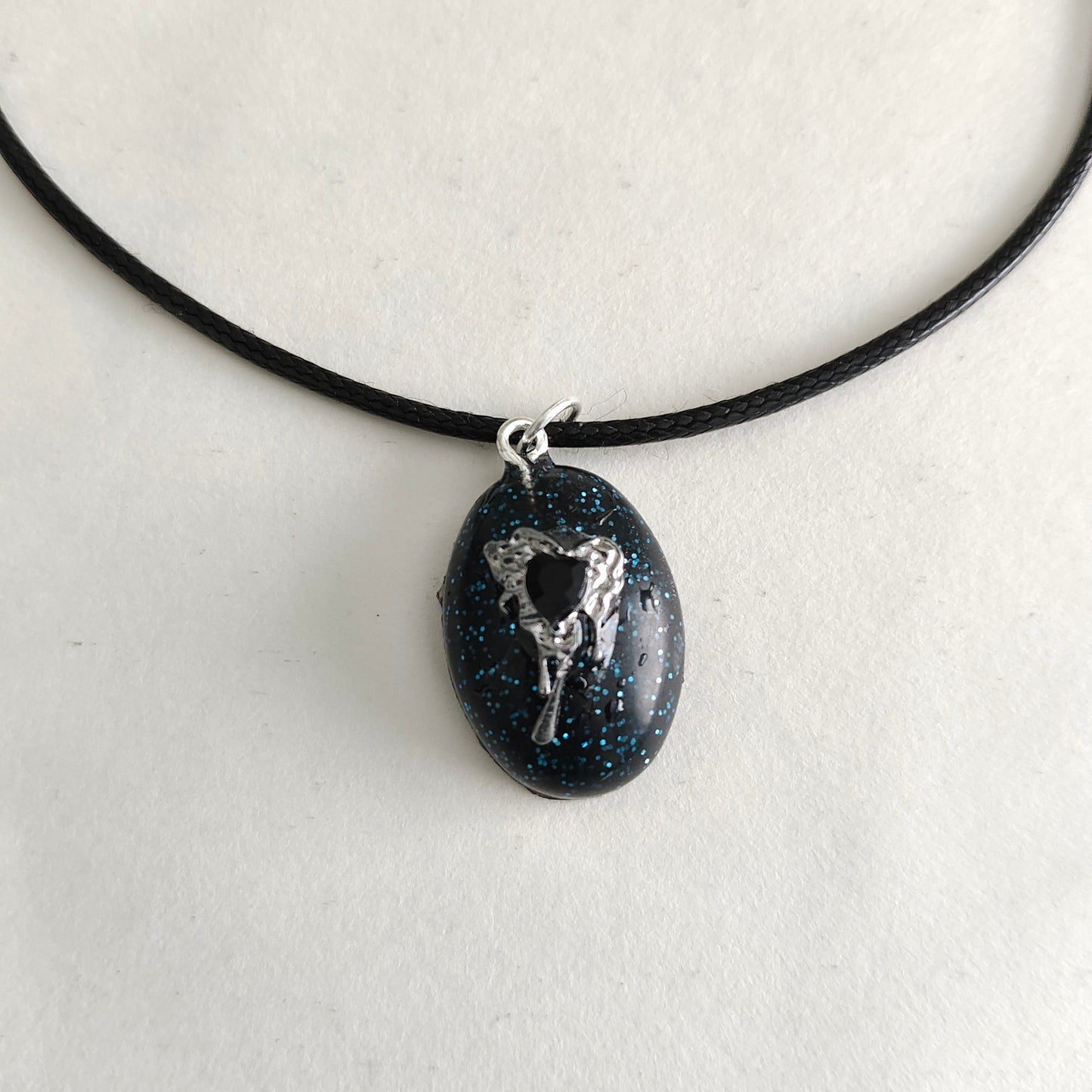 This stunning necklace features a 17.5 inch black waxed cord that is both sleek and durable. The resin and silver charm pendant adds a touch of elegance and charm to any outfit. An effortless way to make a statement.