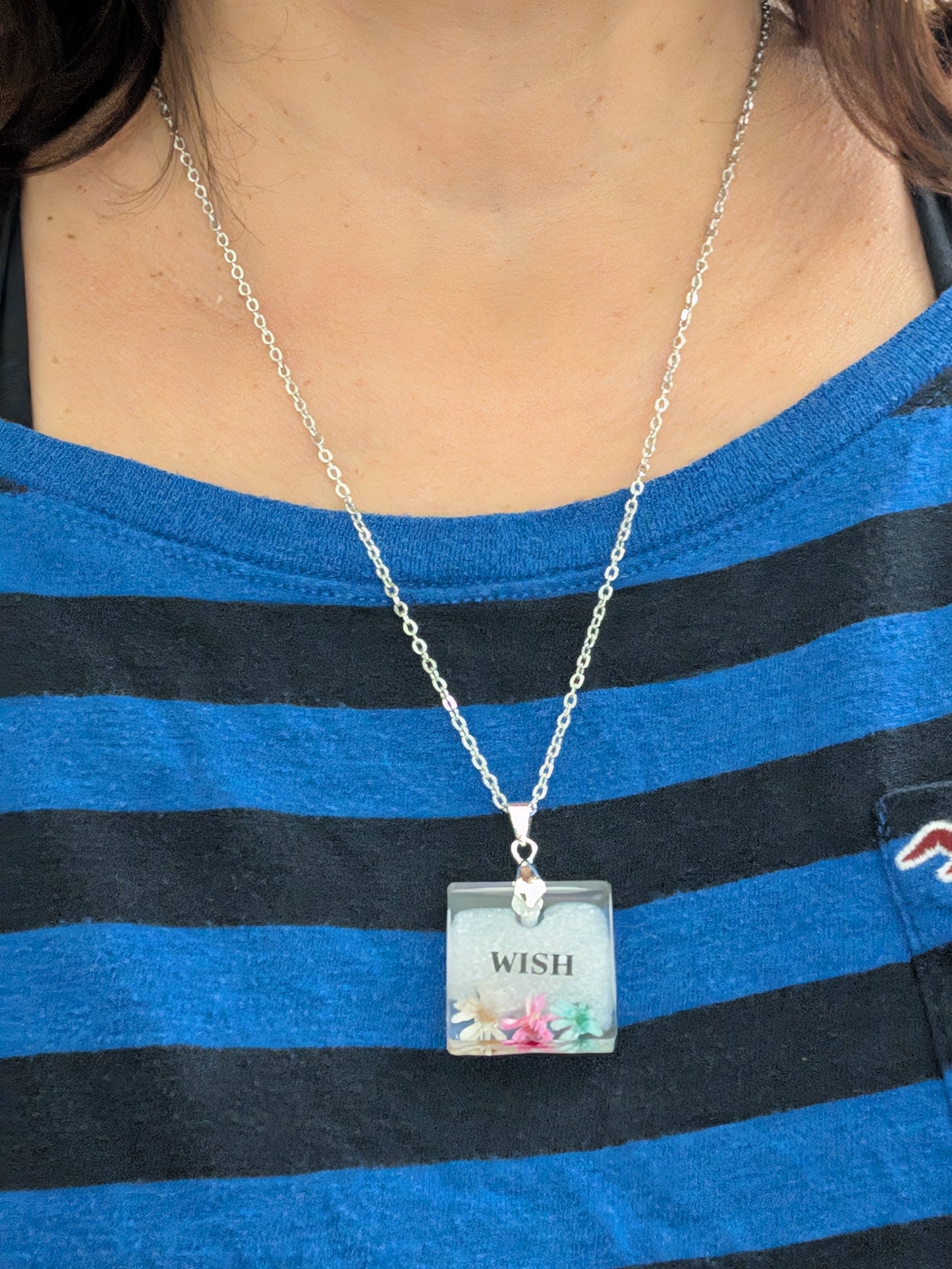 This stainless steel cable link chain necklace features a beautiful square pendant with real flowers embedded in resin. The necklace is 21 inches long, with an additional 2 inch extension chain. Make a statement with this one-of-a-kind piece!

Necklace - 21 inches stainless steel cable link chain with a resin with flowers square pendant
