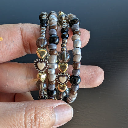 This elegant memory wire bracelet features four coils adorned with black and silver beads, accented by gold hearts and silver spacer beads. Its flexible design ensures a comfortable fit for any wrist size, making it a versatile accessory that adds a touch of sophistication to any outfit. Perfect for gifting or personal wear, this bracelet combines style and ease effortlessly.