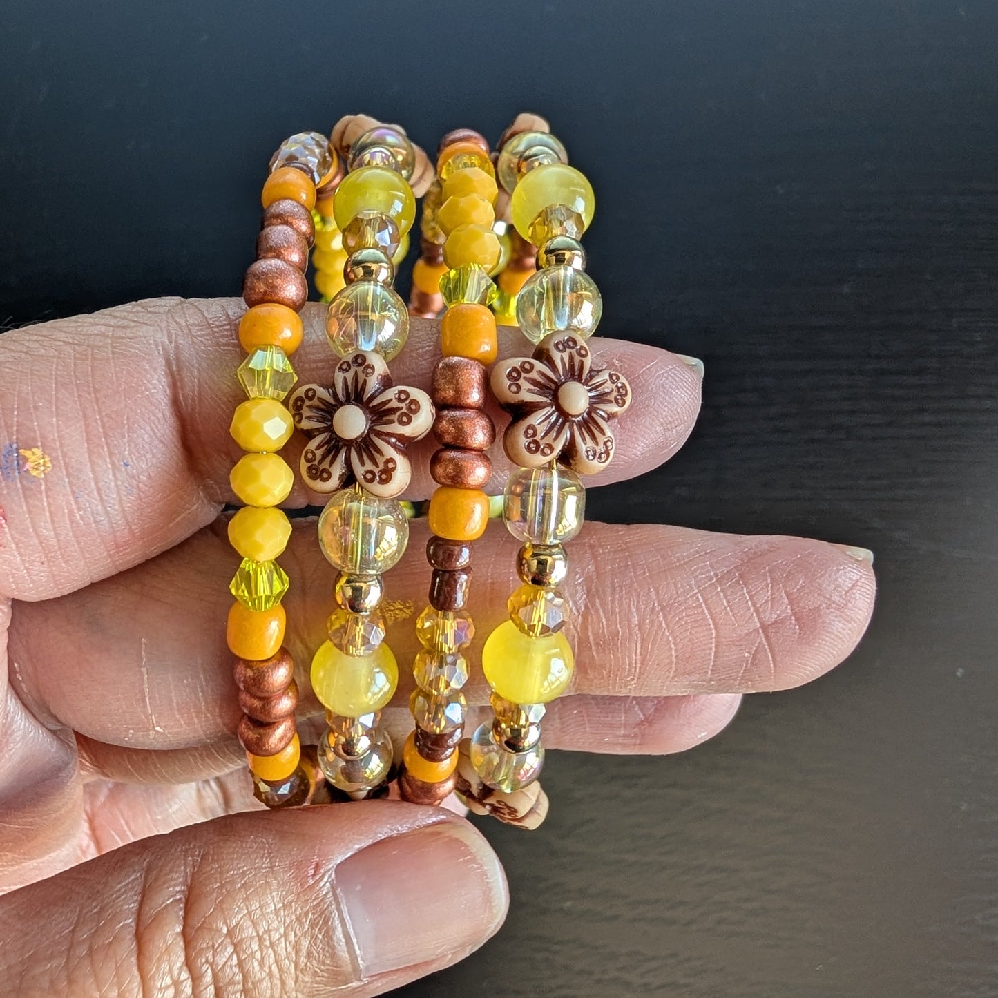 Brighten your style with this stunning memory wire bracelet featuring four coils of vibrant yellow beads accented by yellow and bronze spacer beads. Its flexible design ensures a comfortable fit for any wrist, while the floral-inspired arrangement adds a cheerful, handcrafted touch. Perfect for elevating everyday outfits with a splash of sunny elegance and subtle metallic charm.