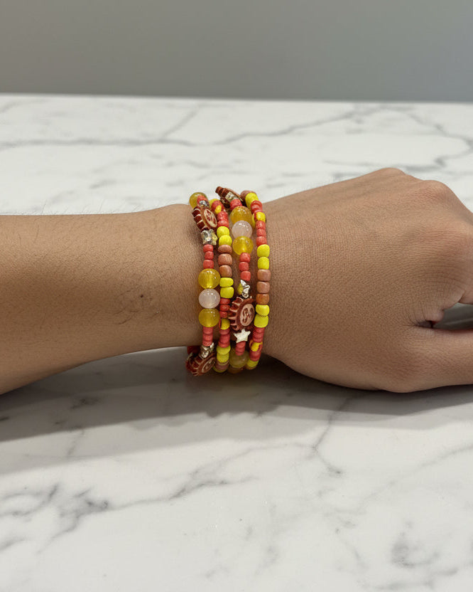 This vibrant memory wire bracelet features four coils adorned with yellow and sun beads, complemented by yellow, tan, and orange spacer beads. Its flexible design ensures a comfortable fit for any wrist size, making it an eye-catching accessory that brightens your look with warm, sunny hues. Perfect for adding a splash of color and effortless style to your everyday outfits.