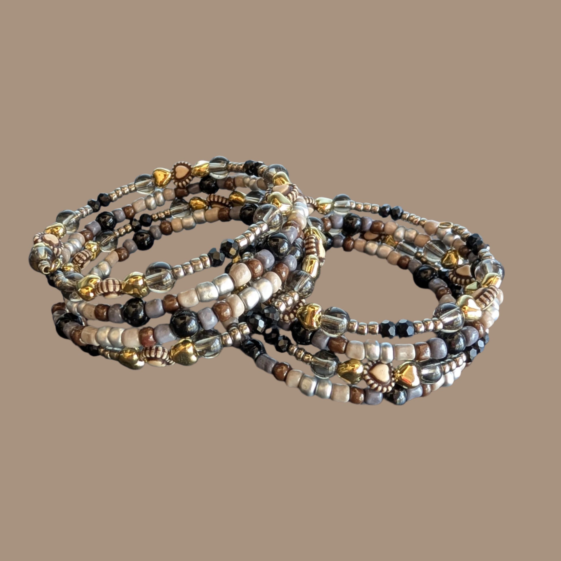 This elegant memory wire bracelet features four coils adorned with black and silver beads, accented by gold hearts and silver spacer beads. Its flexible design ensures a comfortable fit for any wrist size, making it a versatile accessory that adds a touch of sophistication to any outfit. Perfect for gifting or personal wear, this bracelet combines style and ease effortlessly.
