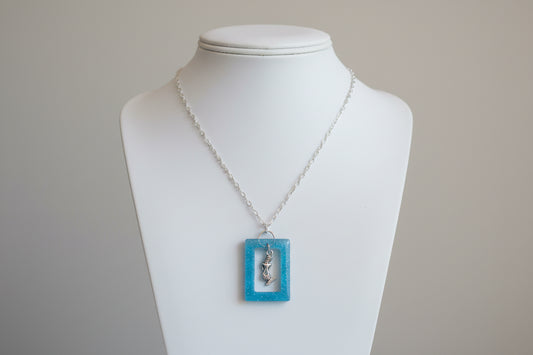Necklace with a blue square pendant featuring a silver mermaid design on a white background