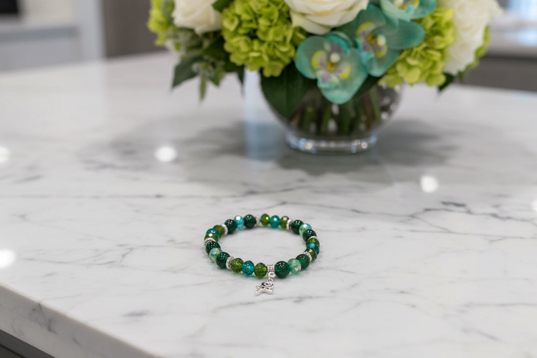 Green beaded bracelet on a marble surface with flowers in the background