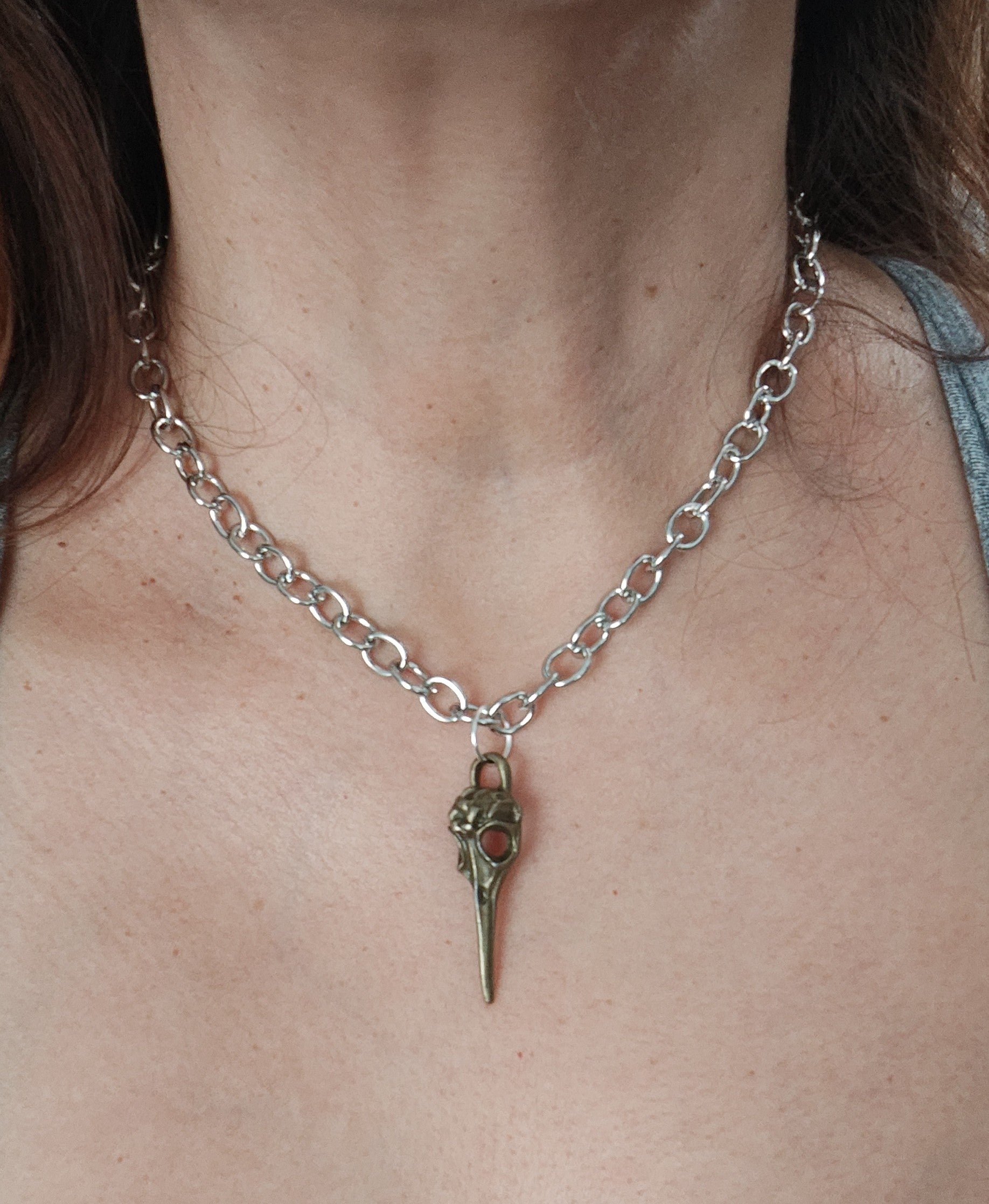 Add some edgy style to your look with our 16" silver chain necklace featuring a unique bronze raven skull head charm. Stand out from the flock with this bold and playful accessory.