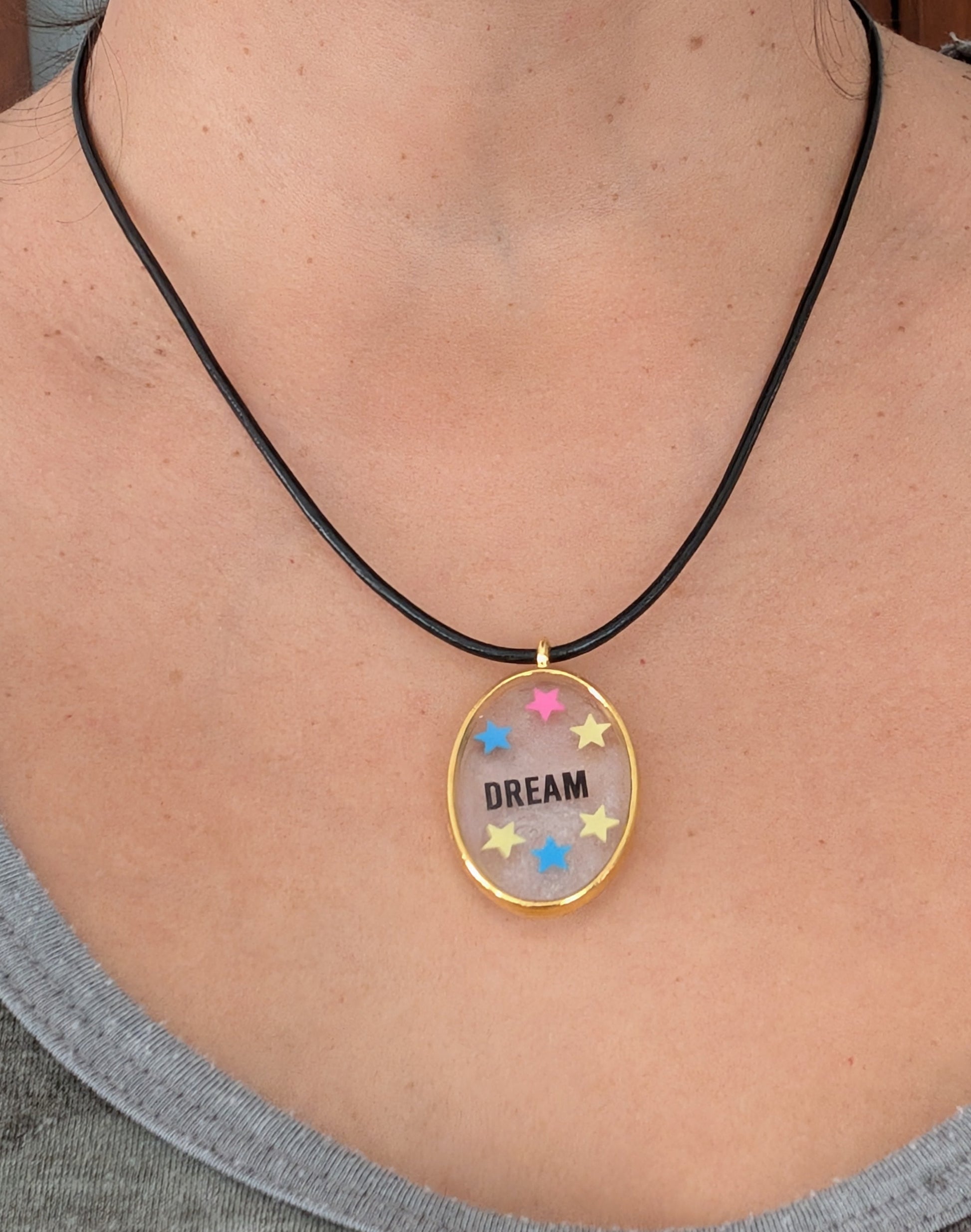 Indulge in the dreamy beauty of our 18 inch resin and stars gold oval pendant necklace. The stunning design is complemented by a 2mm black leather cord and adjustable extension chain. Weighing only 0.2 oz, it's lightweight and comfortable to wear. Elevate your style with this unique and charming accessory.