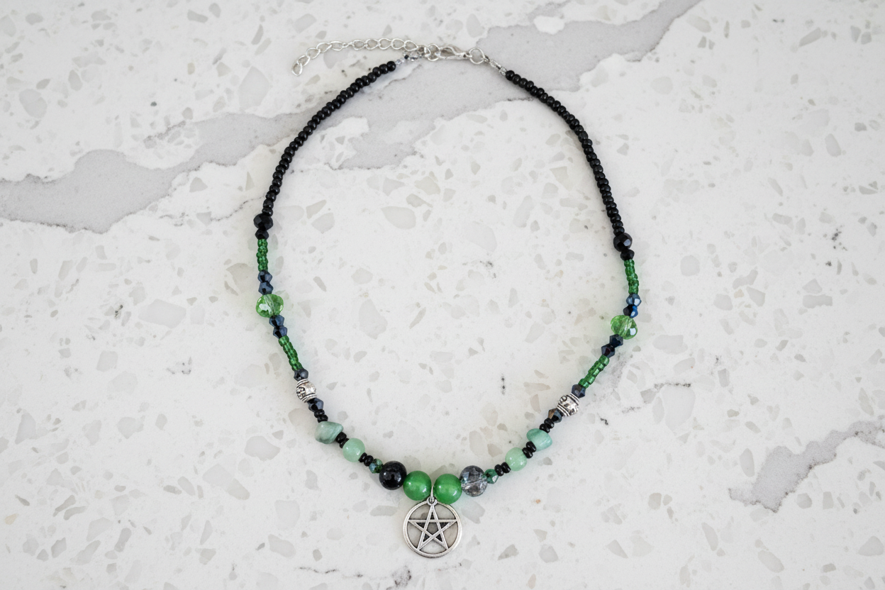 Necklace with green and black beads and a pentacle charm on a textured white surface