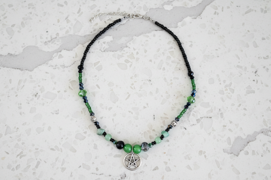 Necklace with green and black beads and a pentacle charm on a textured white surface