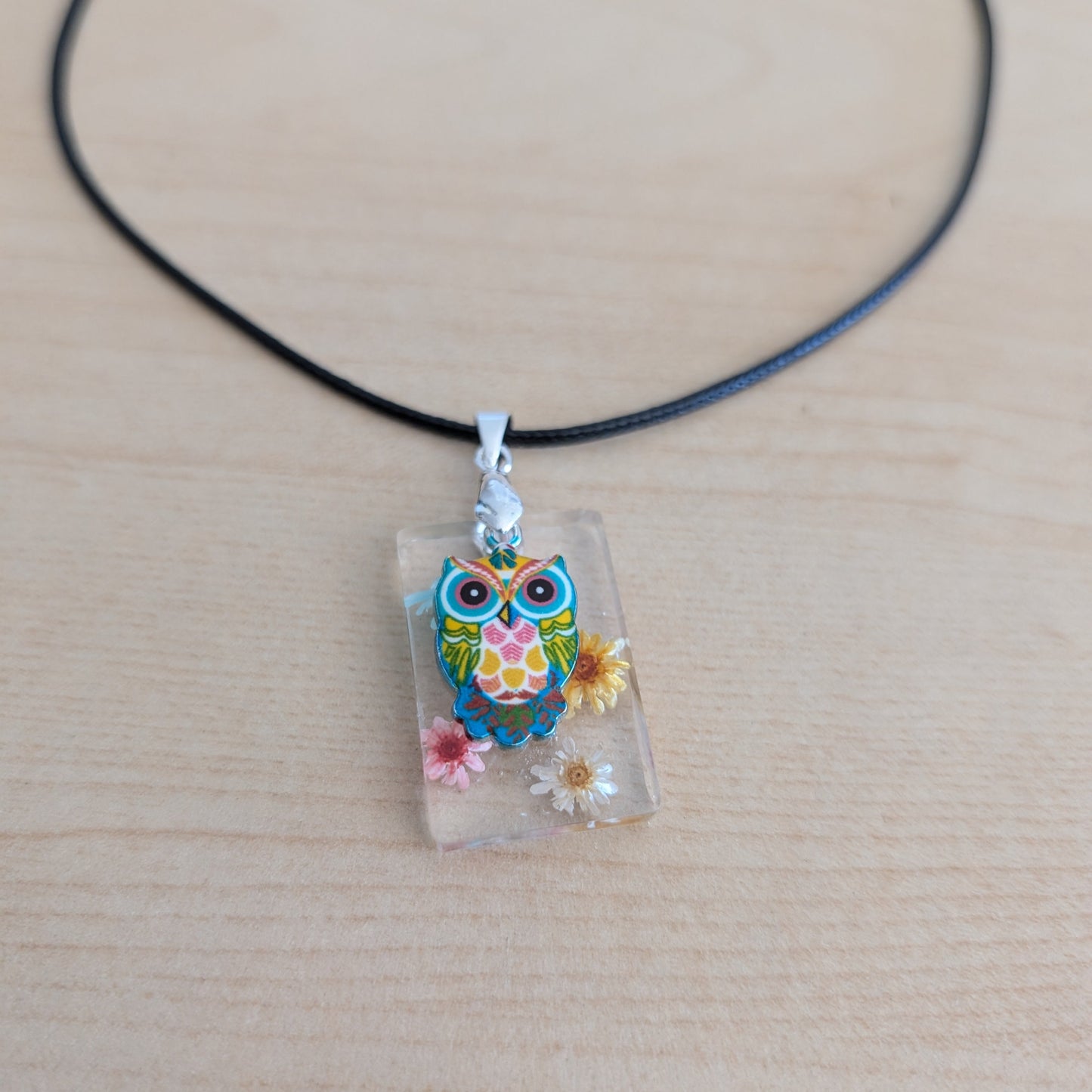 This 17.5-inch necklace features a unique rectangular resin pendant embedded with delicate flowers, paired with a charming silver owl accent. Suspended on a sleek black leather cord with a secure clasp, it combines natural beauty and subtle elegance, making it a perfect accessory to enhance any outfit.