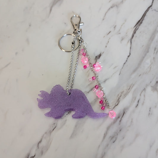 Purple triceratops dinosaur bag charm with pink beads on a marble background