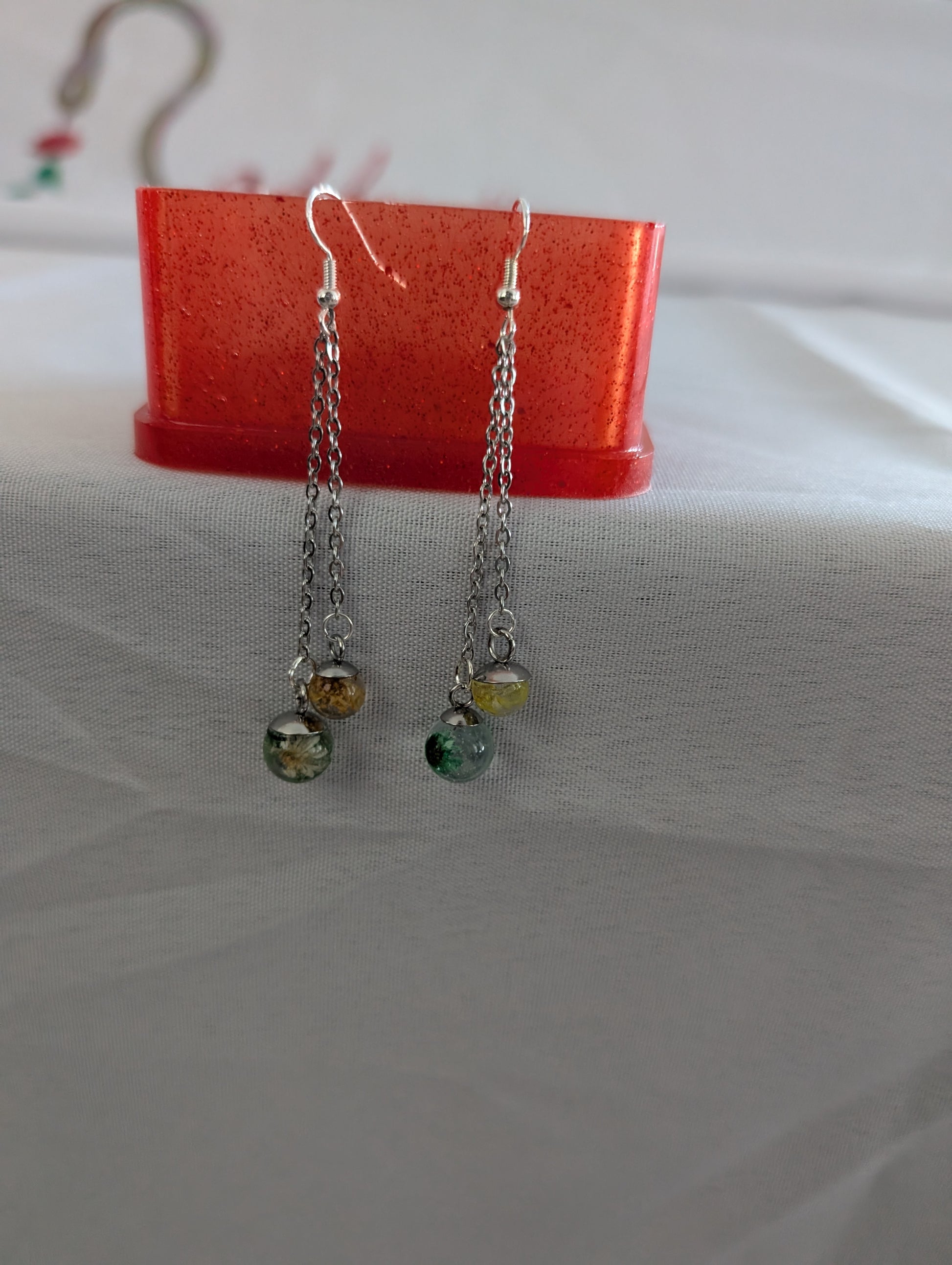Pair of silver chain earrings with colored beads on a red stand.