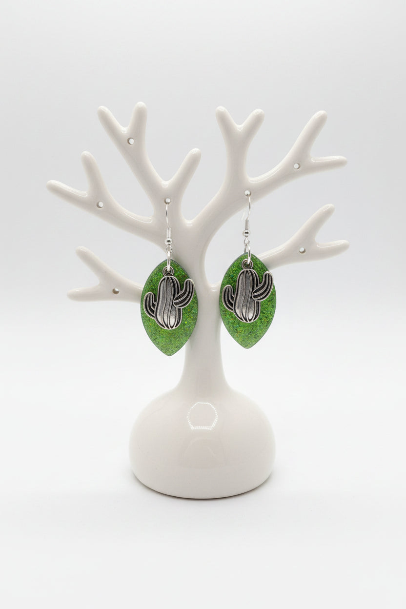 Green leaf-shaped earrings with silver cactus charm  on a marble surface