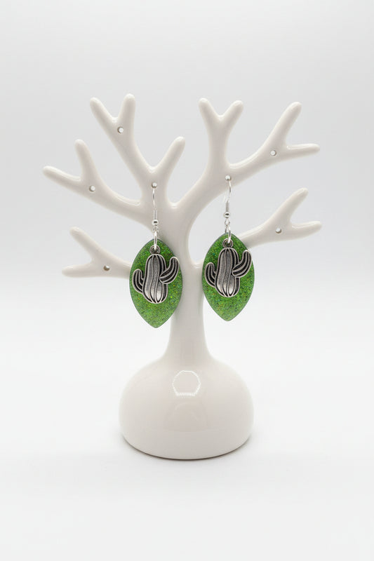 Green leaf-shaped earrings with silver cactus charm  on a marble surface