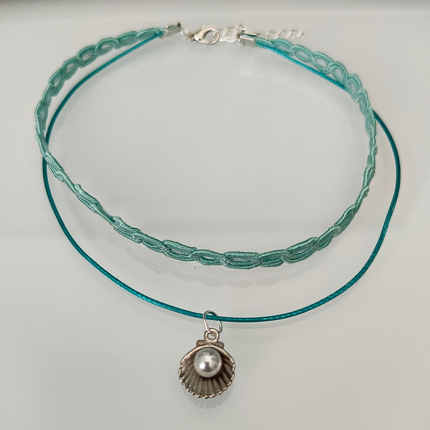 Elevate your style with our stunning Choker Necklace! The aqua lace ribbon, paired with a delicate polyester strand, creates a unique and elegant look. Adorned with a charming clam shell and an acrylic white pearl bead, this necklace exudes sophistication and grace. Stand out from the crowd with this must-have accessory.