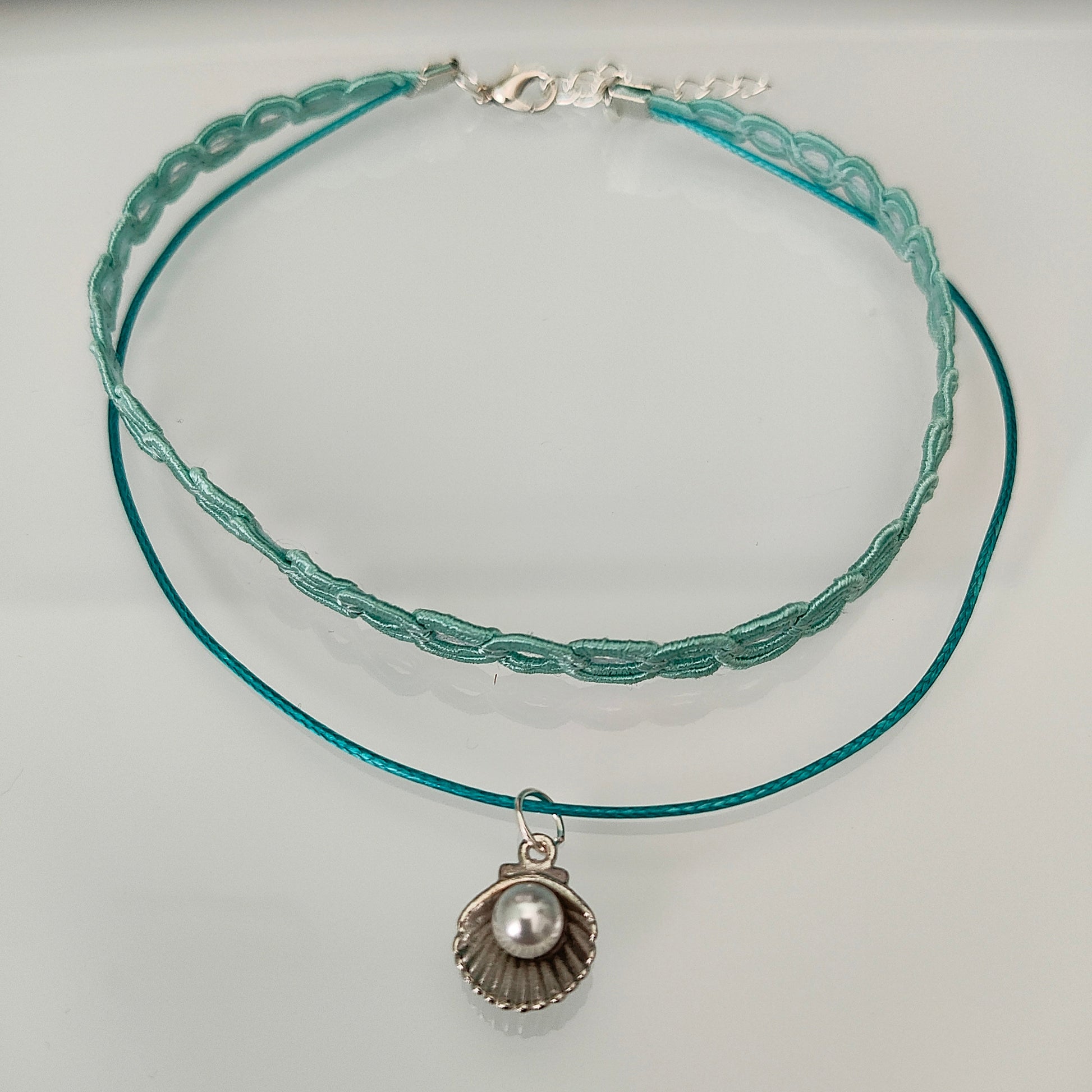 Elevate your style with our stunning Choker Necklace! The aqua lace ribbon, paired with a delicate polyester strand, creates a unique and elegant look. Adorned with a charming clam shell and an acrylic white pearl bead, this necklace exudes sophistication and grace. Stand out from the crowd with this must-have accessory.