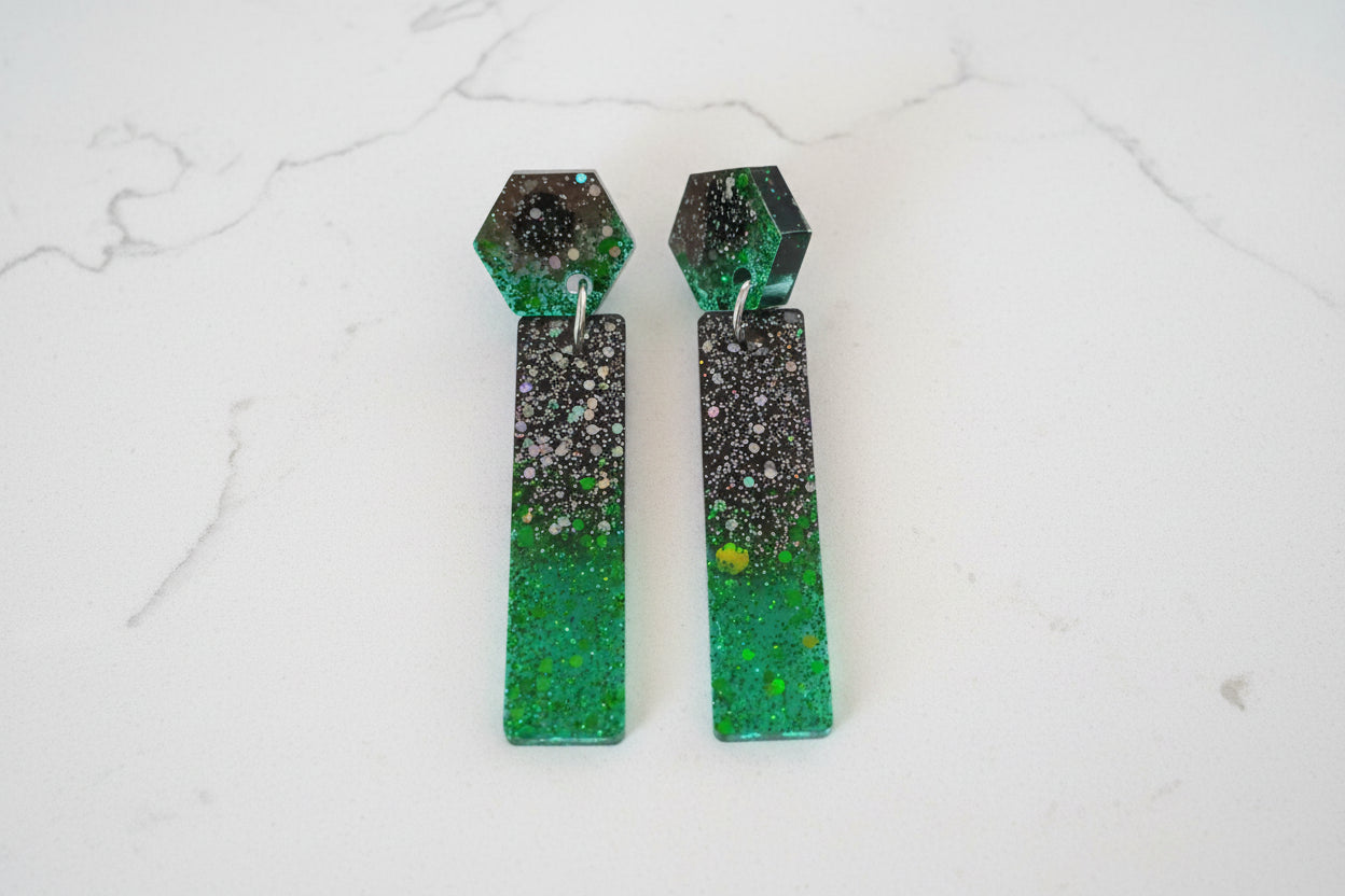Green and black speckled earrings on a white marble background
