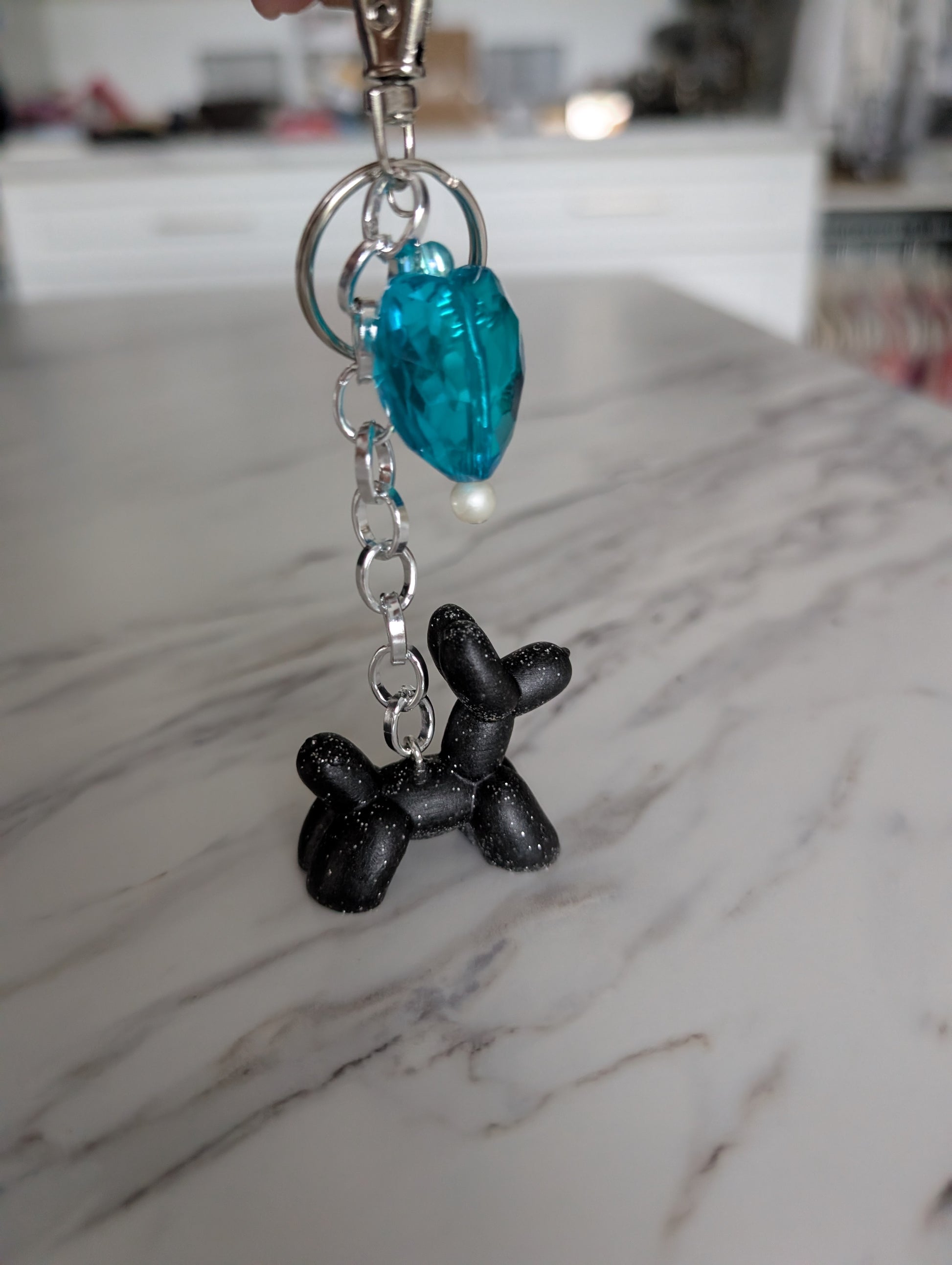 Keychain with black balloon dog charm and blue heart-shaped charm on a marble surface.