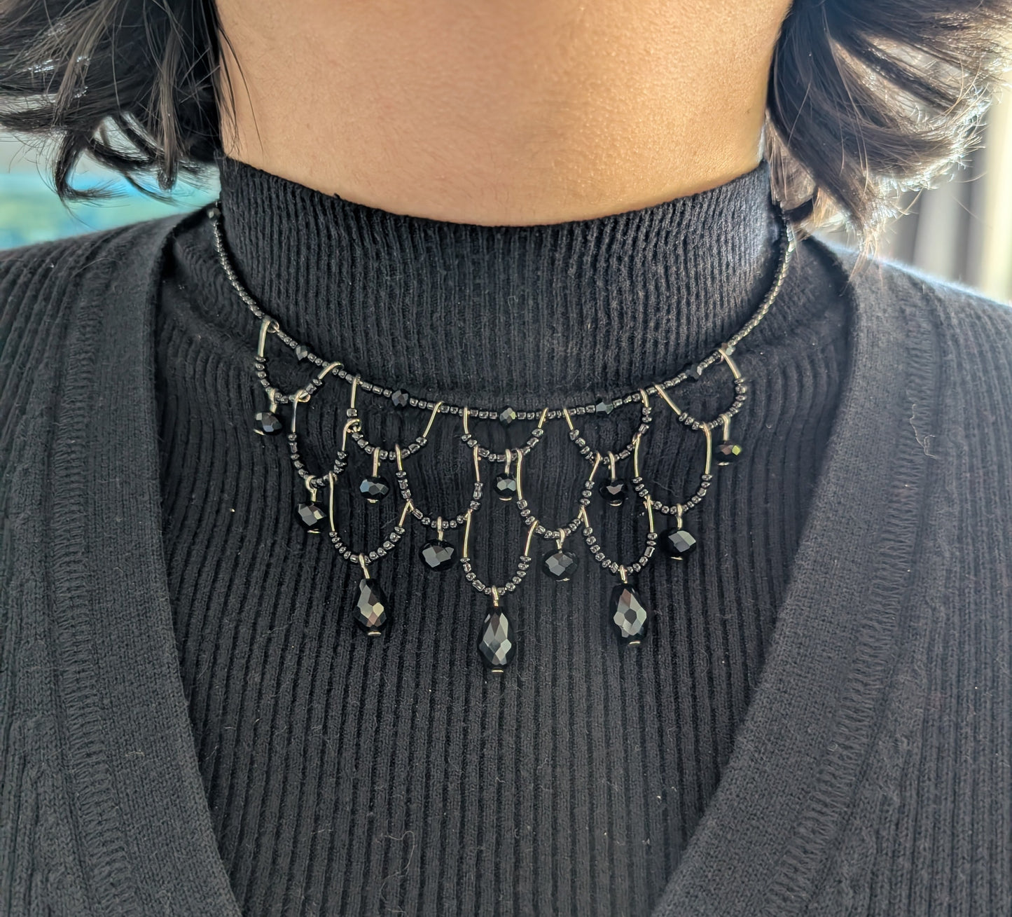 Person wearing a black turtleneck sweater with a decorative black bead choker necklace.