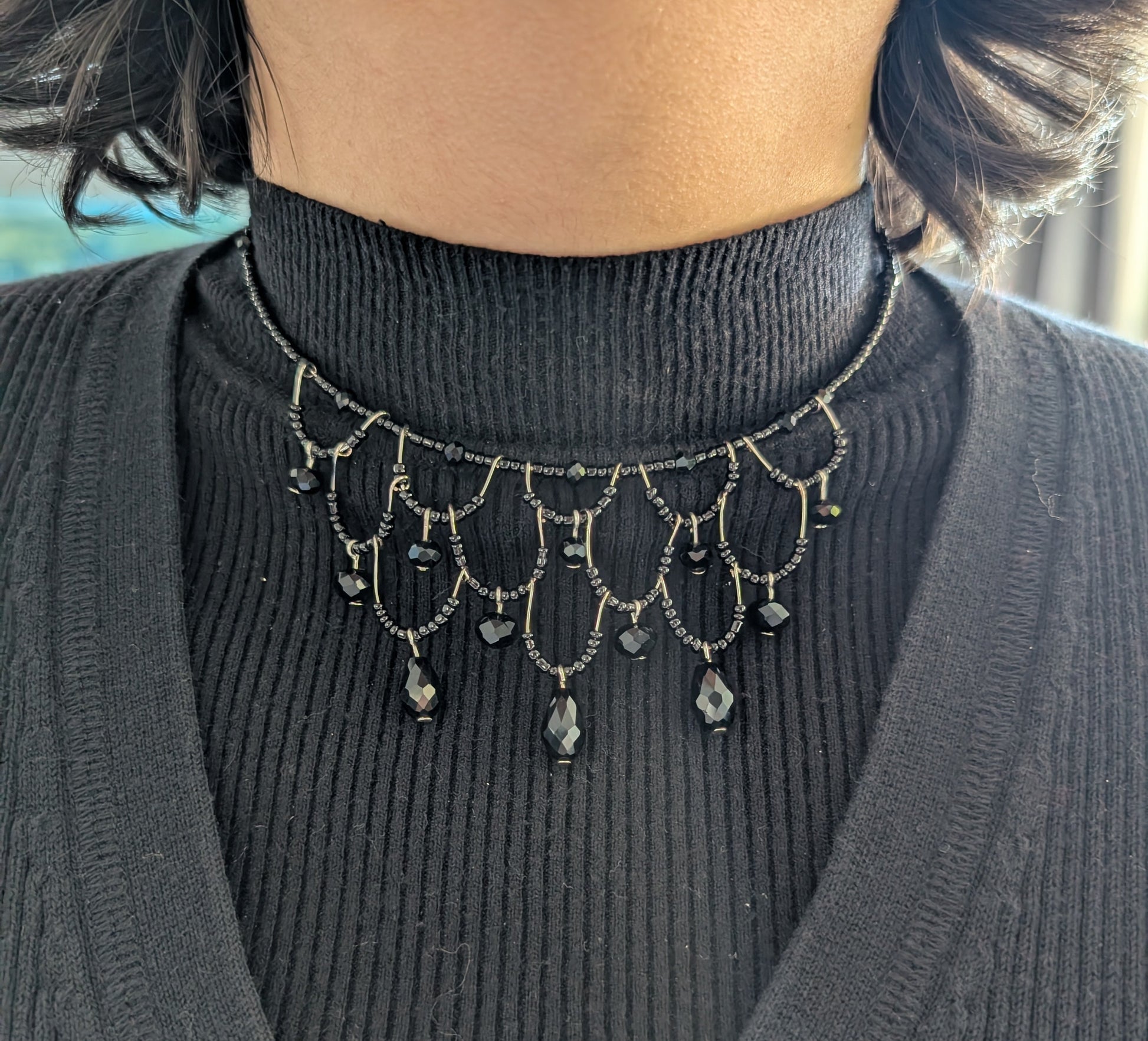 Person wearing a black turtleneck sweater with a decorative black bead choker necklace.